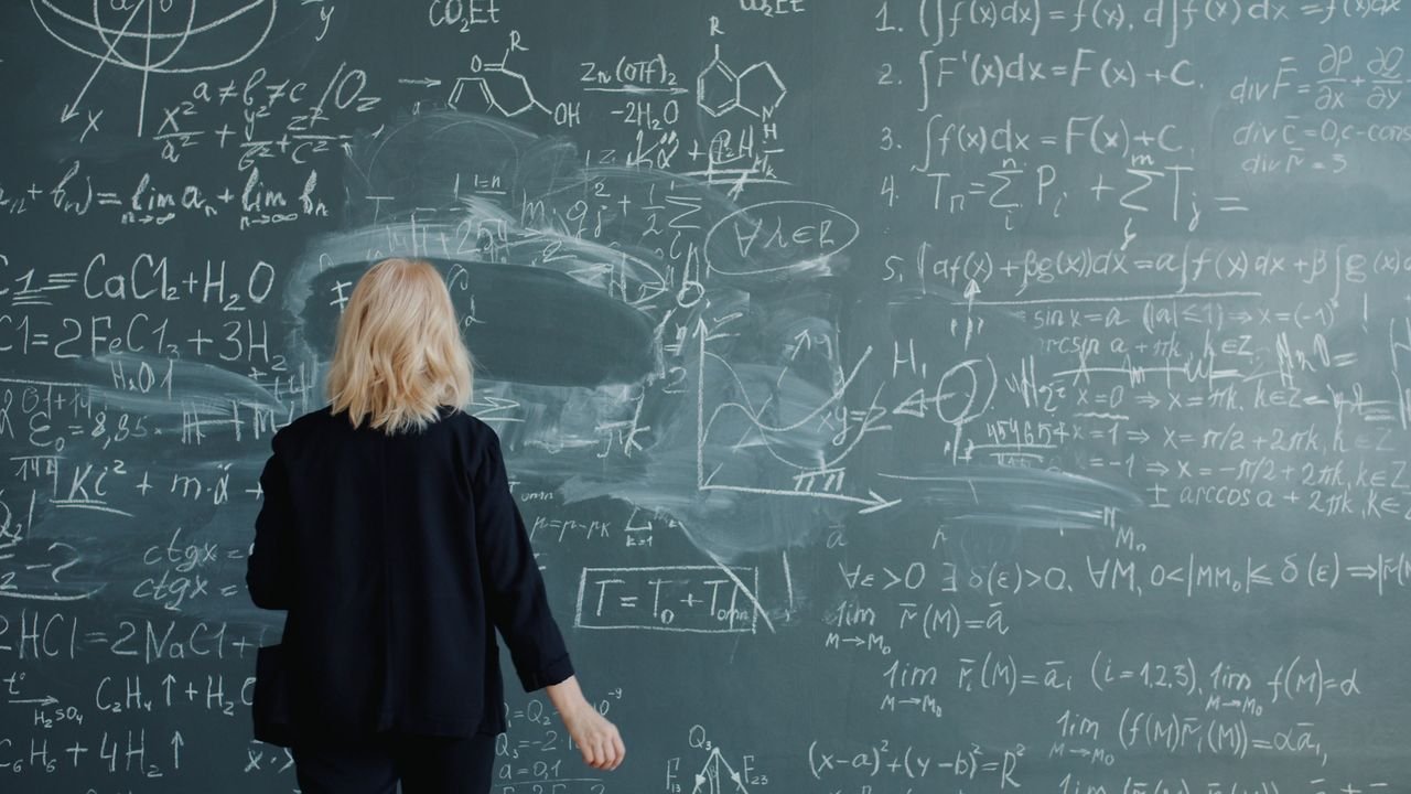 The Art of Drawing Readers In: Your attractive post title goes here Woman writing on chalkboard filled with complex mathematical equations.