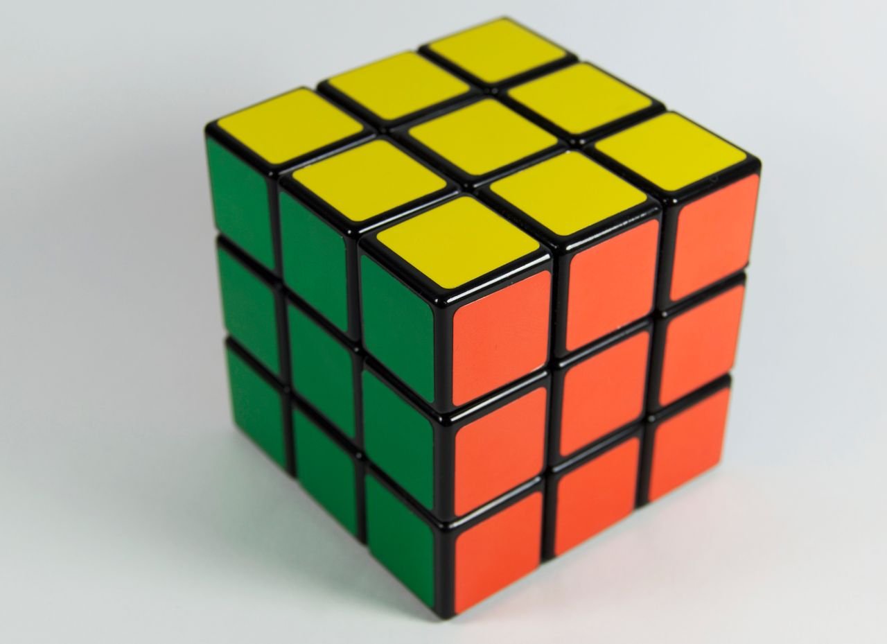 Services A solved Rubik's Cube displaying red, yellow, and green colors on a white backdrop. Perfect for puzzle enthusiasts.